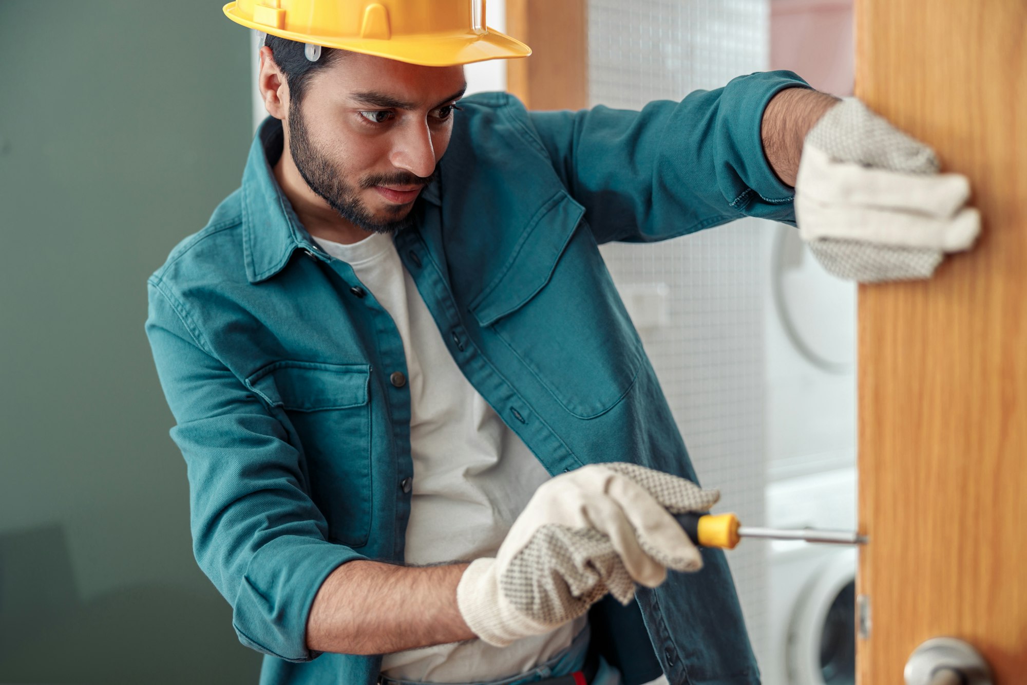 Focused Locksmith workman in uniform installing door knob. Professional repair service